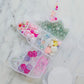 Little Miss Unicorn Bead Kit featuring glitter alphabet beads, iridescent star and heart beads, and various other beads, along with pink and clear string. Perfect for creating custom bracelets or necklaces. WARNING: Contains small parts. Made by women-owned small business, STACKS!