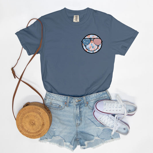 Retro smiley face sunglasses t-shirt featuring a patriotic design with American flag shades. Perfect for 4th of July celebrations, this vintage-style Comfort Colors tee is soft-washed, pre-shrunk, and available in unisex sizes. Show off 90s nostalgia with this fun and comfortable USA flag shirt, ideal for summer BBQs, fireworks, and family gatherings.