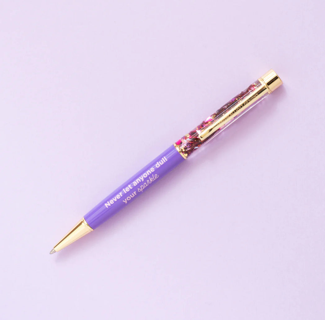 Confetti pen with gold metal accents, imprinted with 'Never let anyone dull your sparkle.' Medium ballpoint pen with black ink and a twist tip. Perfect desk accessory or gift, pairs well with notebooks. Features water-filled liquid inside for extra sparkle.