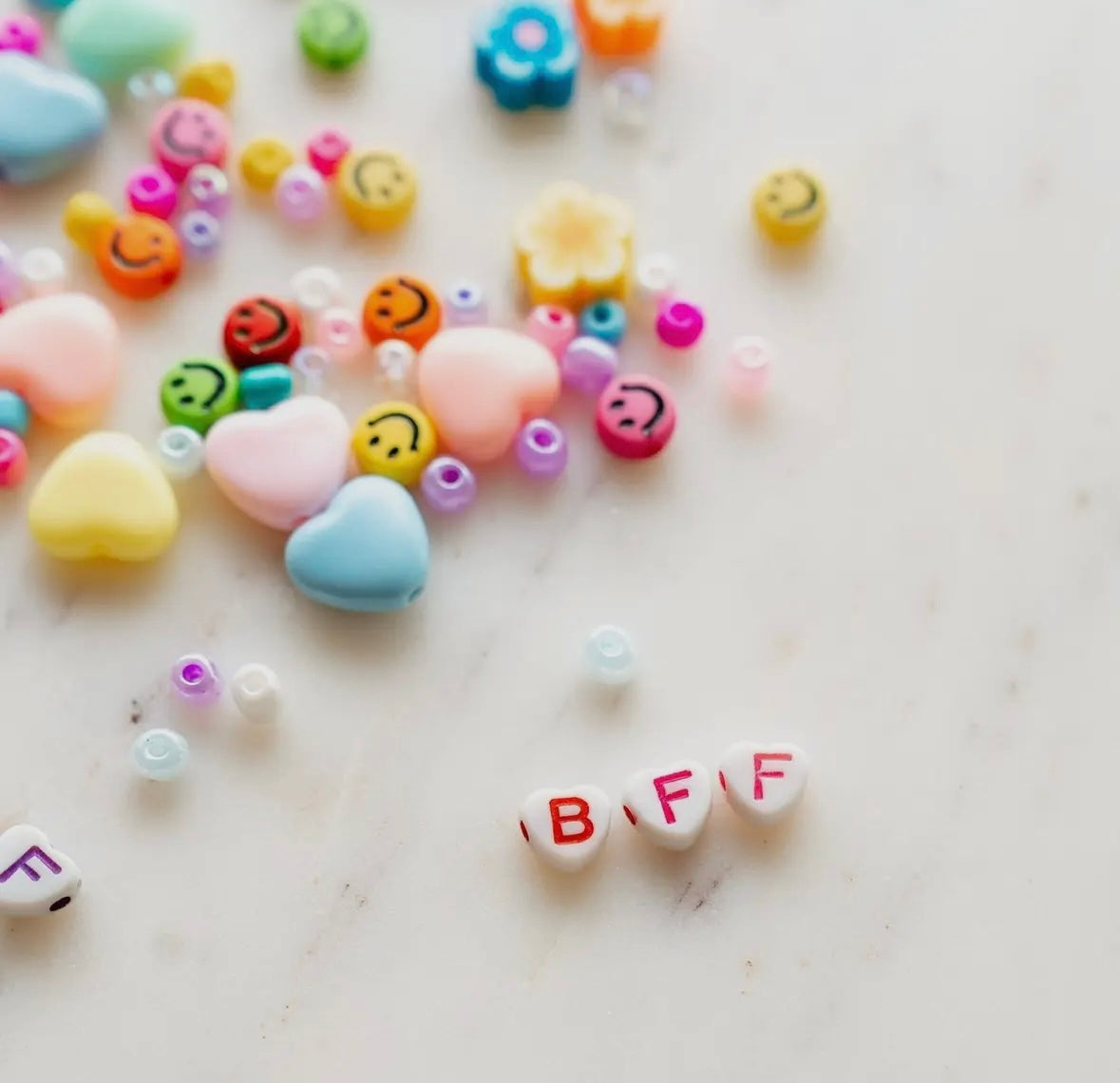 Rainbow heart and smiley face letter beads for DIY bracelet making. Includes assorted beads, clear string, and options for personalized names. Perfect for camp, slumber parties, or school crafts.