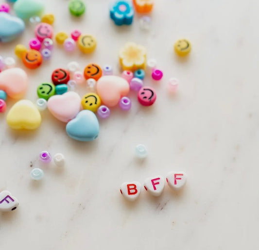 Rainbow heart and smiley face letter beads for DIY bracelet making. Includes assorted beads, clear string, and options for personalized names. Perfect for camp, slumber parties, or school crafts.