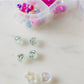 Little Miss Unicorn Bead Kit featuring glitter alphabet beads, iridescent star and heart beads, and various other beads, along with pink and clear string. Perfect for creating custom bracelets or necklaces. WARNING: Contains small parts. Made by women-owned small business, STACKS!