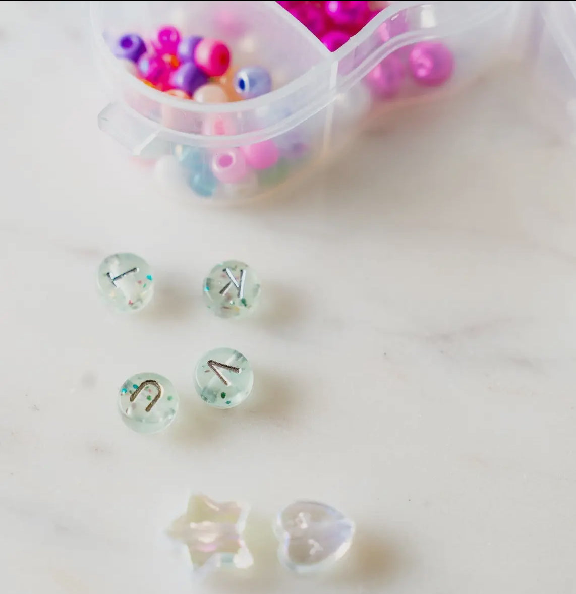 Little Miss Unicorn Bead Kit featuring glitter alphabet beads, iridescent star and heart beads, and various other beads, along with pink and clear string. Perfect for creating custom bracelets or necklaces. WARNING: Contains small parts. Made by women-owned small business, STACKS!