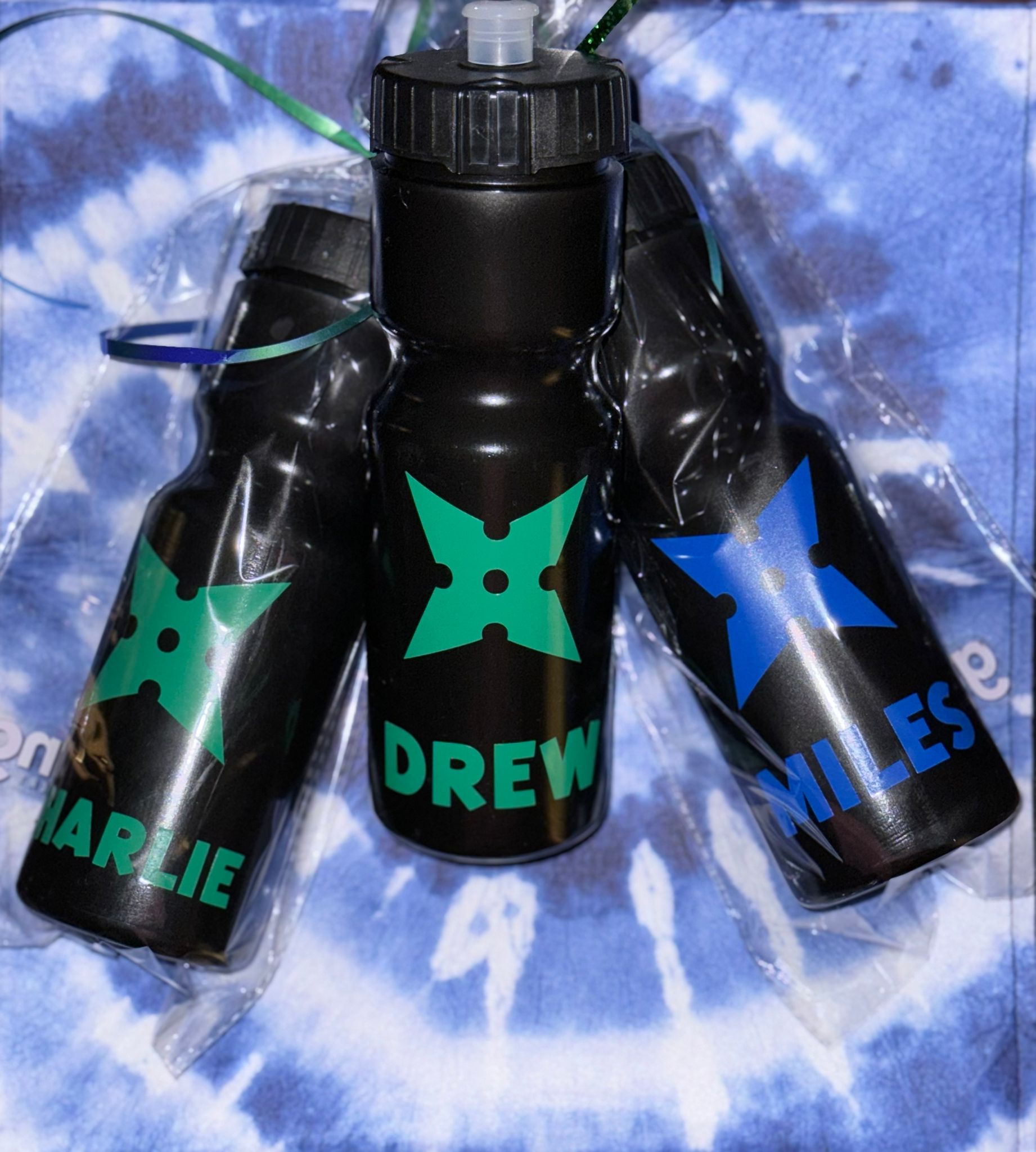 Personalized black hydration bottles with vibrant, ninja-inspired star symbols and names in colorful, glossy or sparkly finishes. Perfect for kids’ birthday parties, school events, or everyday adventures, these durable bottles make unique gifts or party favors. Sleek design, customized for each child, and wrapped with decorative ribbons for easy gifting.