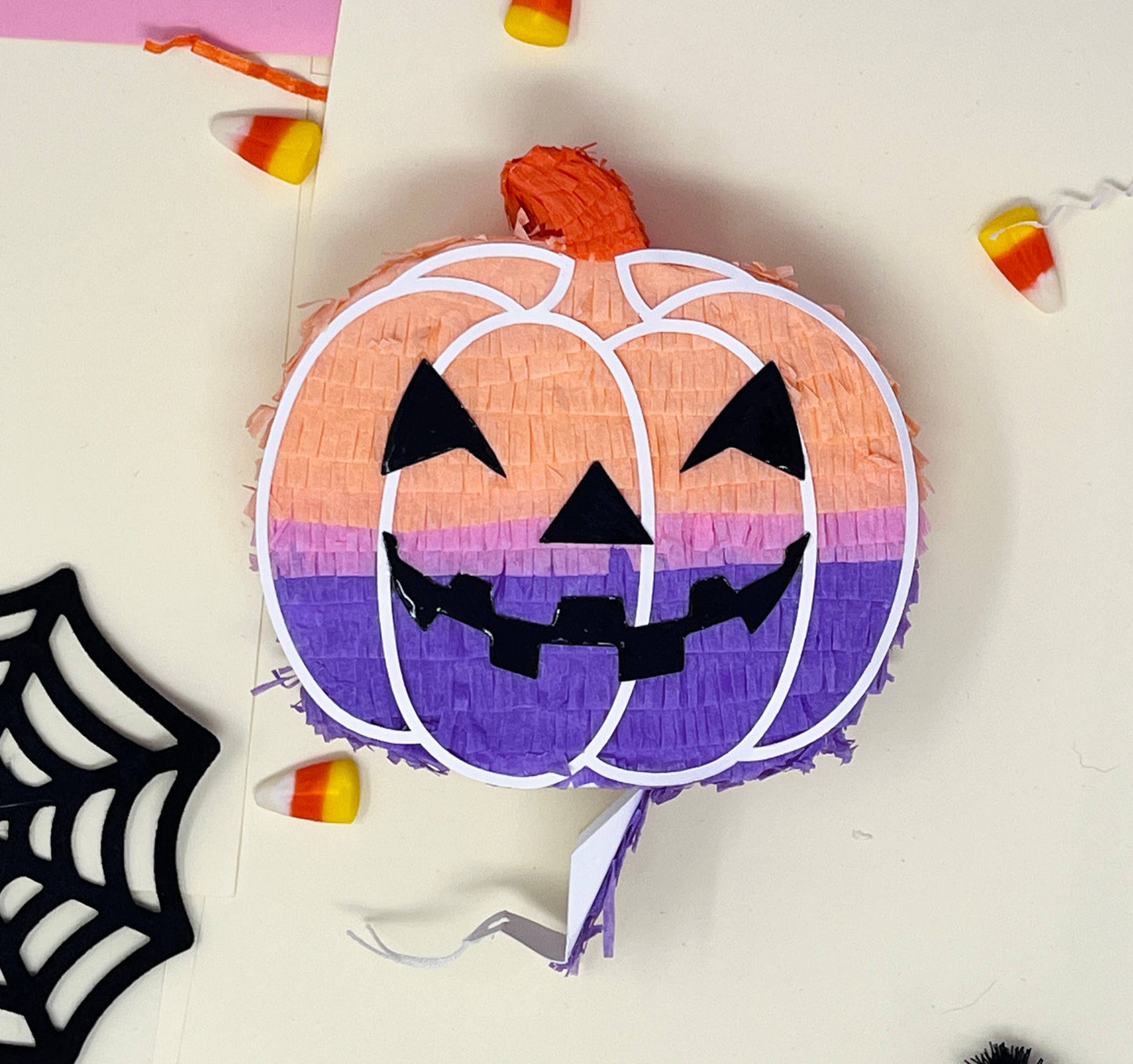 Groovy mini pumpkin piñata with orange, lavender, and pink colors for a boho Halloween vibe. Measures 5 inches tall and long, with a 1.5-inch width, featuring a trap door for treats. Perfect for Halloween decor or party favors for kids and family.