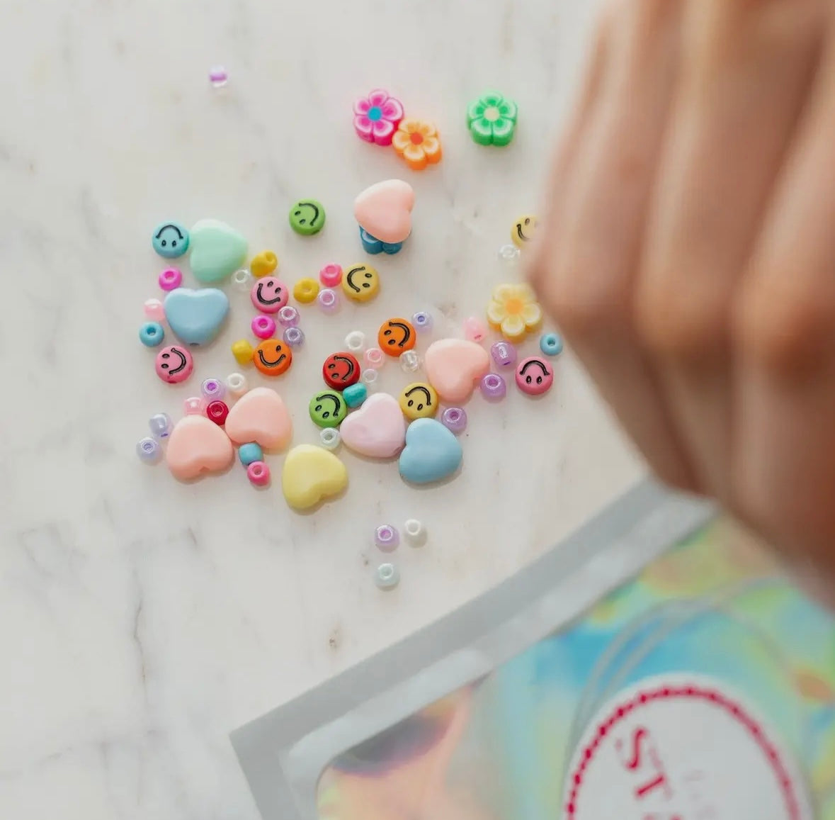 Rainbow heart and smiley face letter beads for DIY bracelet making. Includes assorted beads, clear string, and options for personalized names. Perfect for camp, slumber parties, or school crafts.