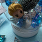 Frozen-themed sensory kit featuring snowy blue/white glitter swirl dough in a snow globe, Frozen figurines, soft snowy trees, snowmen, and glitter pompoms. Perfect for sensory development and creative play. Ideal for kids 3 and up. Choking hazard warning.