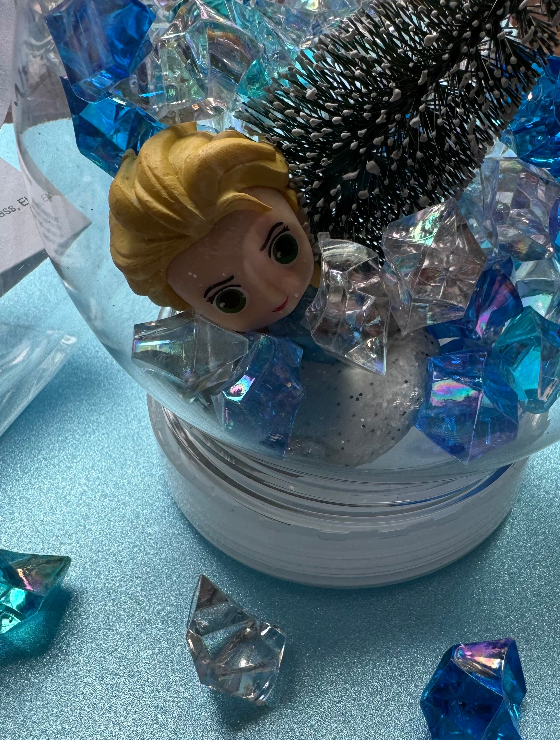 Frozen-themed sensory kit featuring snowy blue/white glitter swirl dough in a snow globe, Frozen figurines, soft snowy trees, snowmen, and glitter pompoms. Perfect for sensory development and creative play. Ideal for kids 3 and up. Choking hazard warning.