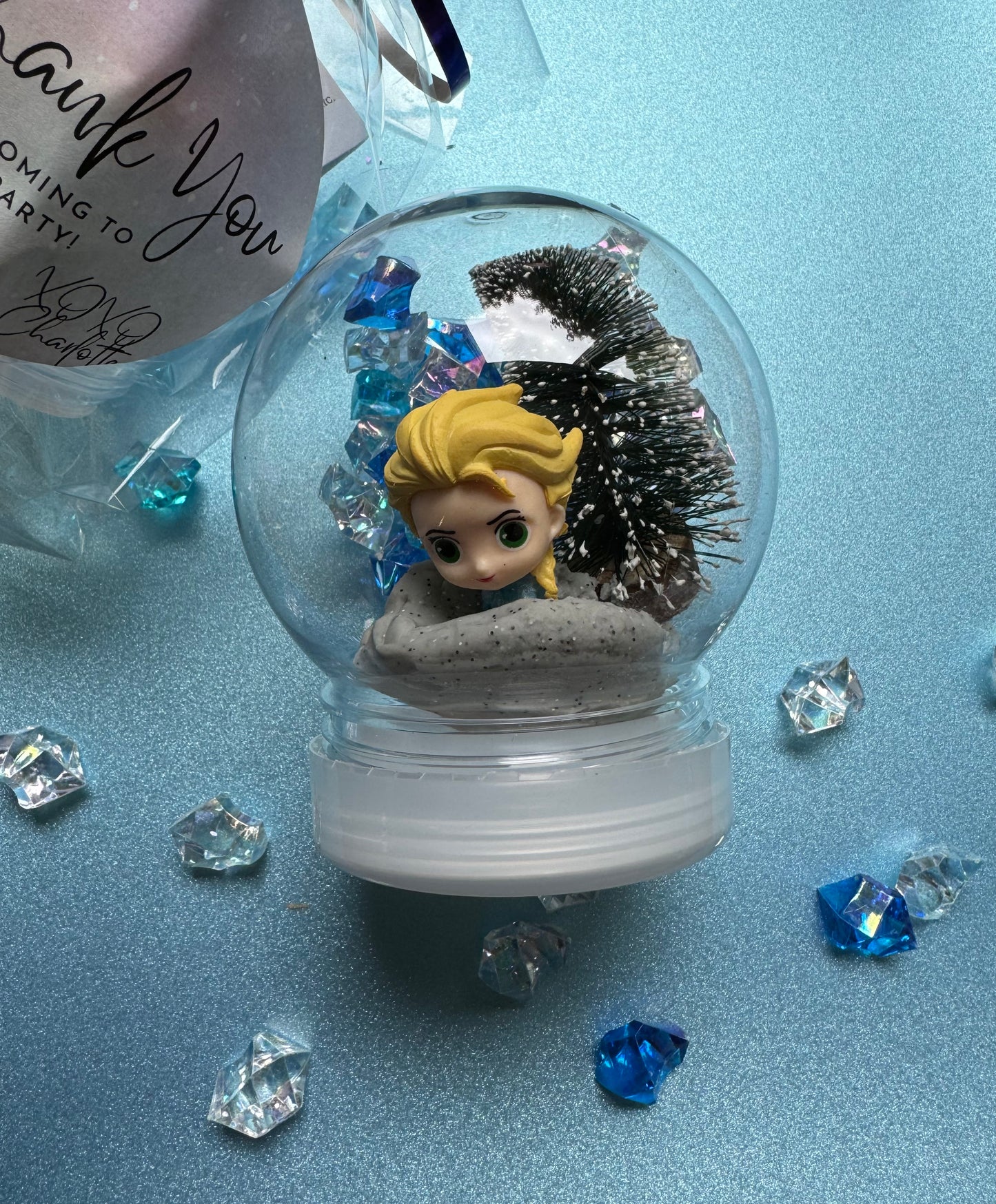 Frozen-themed sensory kit featuring snowy blue/white glitter swirl dough in a snow globe, Frozen figurines, soft snowy trees, snowmen, and glitter pompoms. Perfect for sensory development and creative play. Ideal for kids 3 and up. Choking hazard warning.