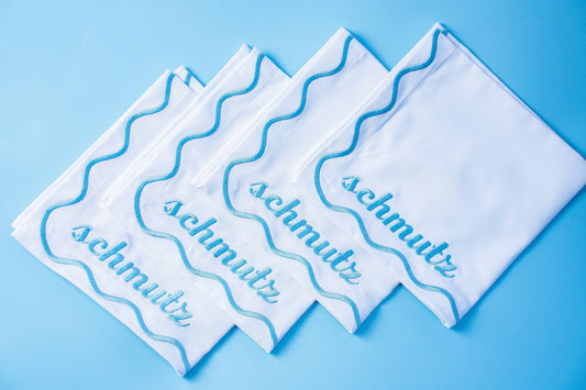 Set of 4 embroidered cotton napkins with a wavy border design, available in Bubbe Blue and Oy Vey Navy. Ideal for dinner parties, these 15-inch napkins are perfect for wiping up schmutz. Machine washable and ready for gifting, wrapped in ribbon.