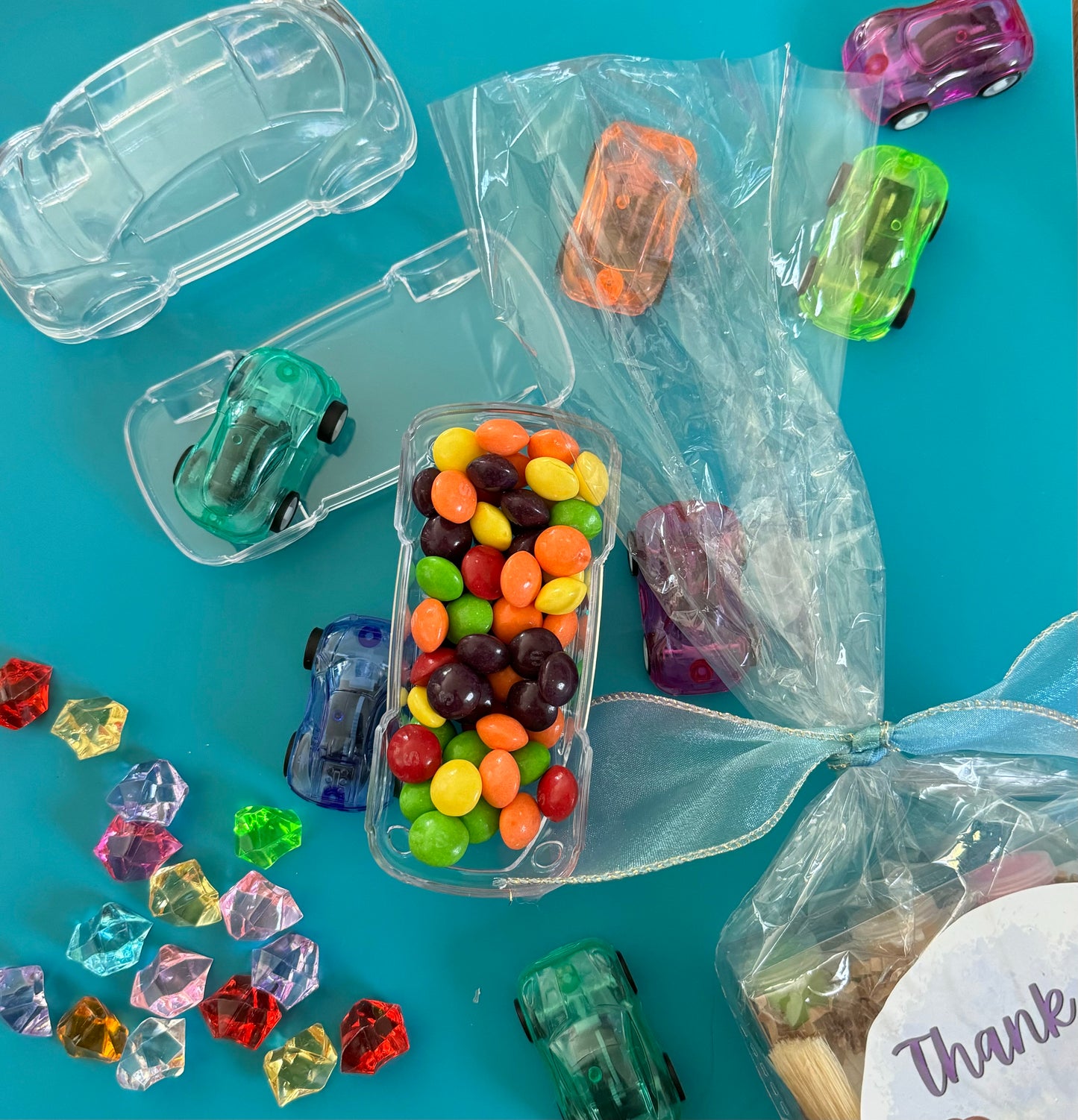 Car-themed candy favors, perfect for birthdays or playdates. Includes car-themed gummies or rainbow Skittles in a car-shaped box. Wrapped in cellophane with optional thank you label. Fun and delicious treat for any party. Custom candy containers available.