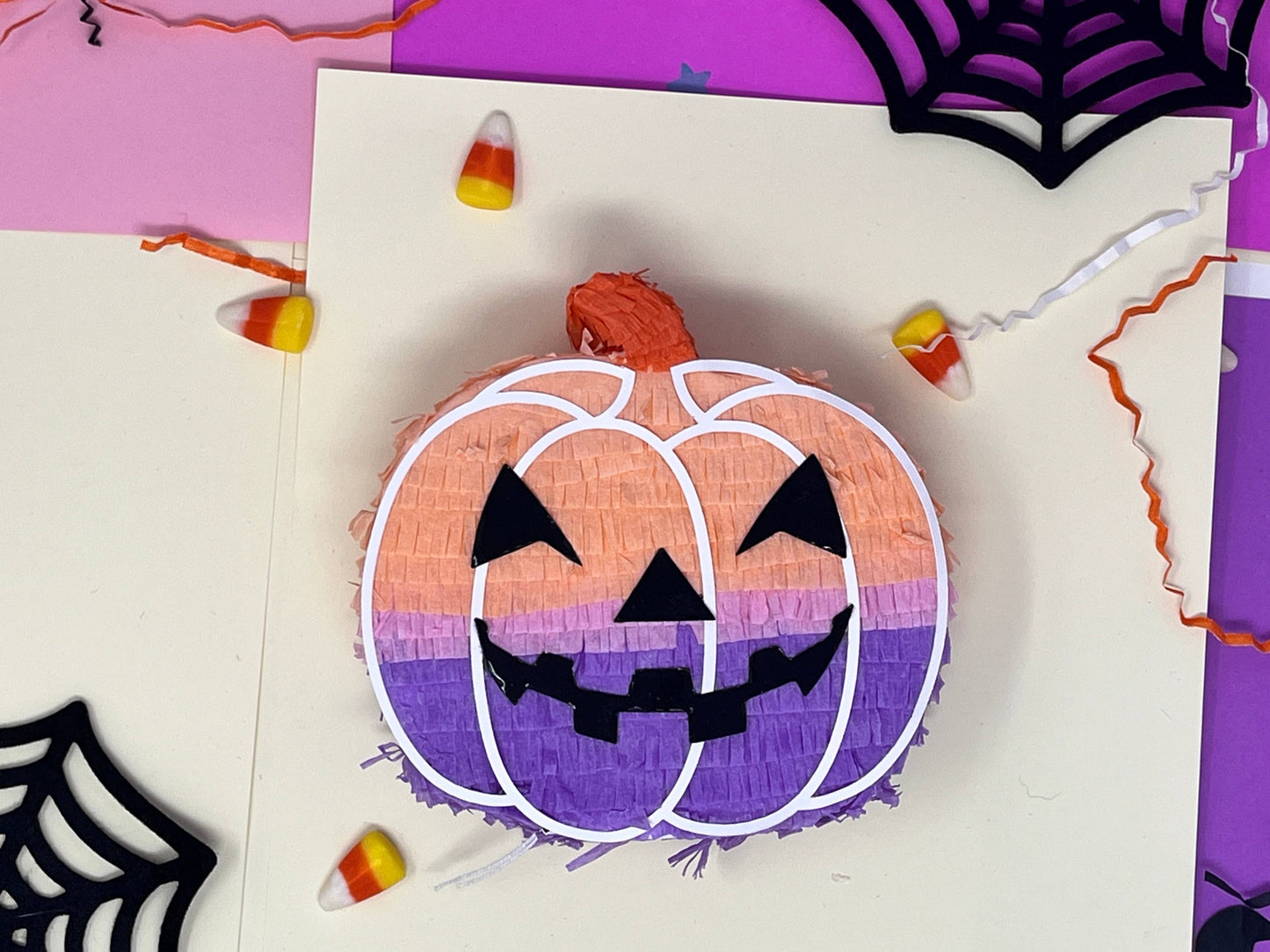 Groovy mini pumpkin piñata with orange, lavender, and pink colors for a boho Halloween vibe. Measures 5 inches tall and long, with a 1.5-inch width, featuring a trap door for treats. Perfect for Halloween decor or party favors for kids and family.