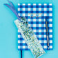 Delightful confetti bookmark for books, planners, or Bibles, measuring 2" x 7". Made of clear plastic with blue and green confetti, finished with a blue gingham ribbon.