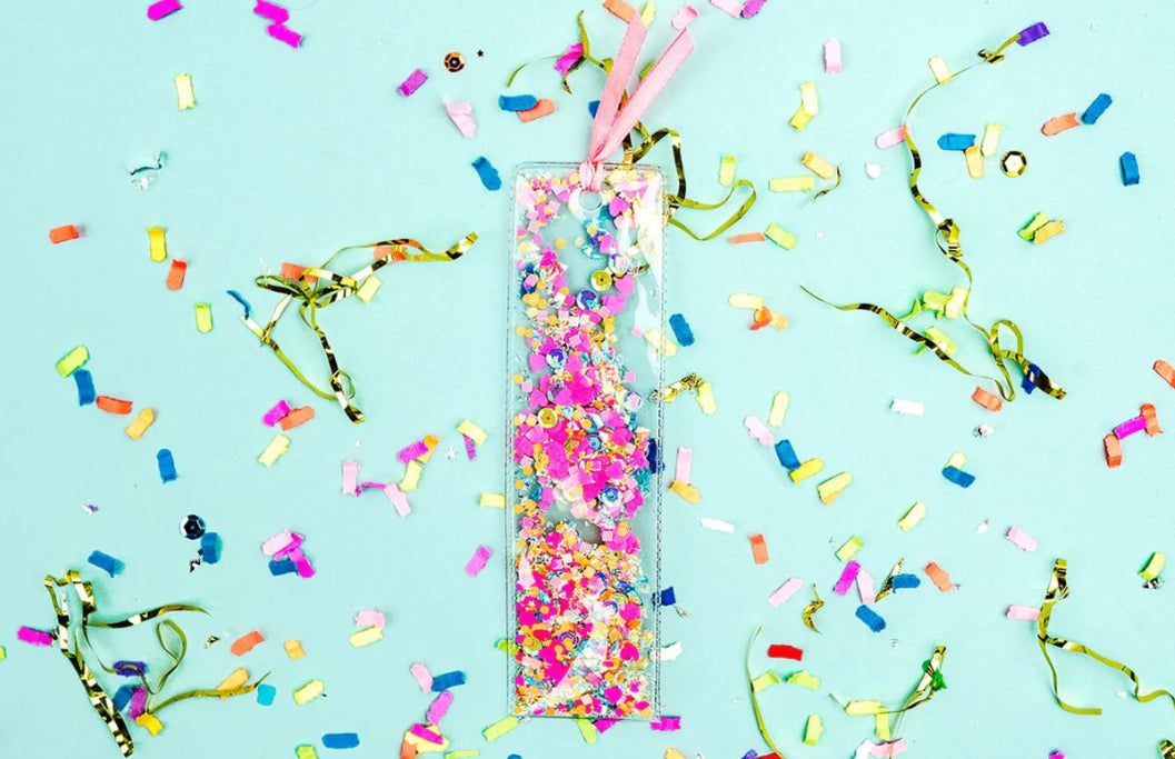 Fun confetti bookmark, perfect for book lovers. Measures 2" x 7", made from clear plastic with hand-selected, colorful confetti inside. Tied with a pink ribbon for an added touch of charm. Imported.