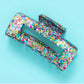 Sparkly 4-inch claw clip featuring colorful confetti, perfect for holding hair securely while adding a touch of style to any outfit. Ideal for everyday wear or special occasions, this durable hair accessory is a must-have for fashion-forward individuals.