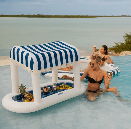 FUNBOY Floating Cabana Bar measuring nearly 6ft long, perfect for outdoor entertainers and summer parties. This inflatable drink station features a navy blue and white cabana stripe fabric sun shade that helps keep drinks and ice cold. With dual circular drink holders for ice or beverages and four additional cup holders, it’s ideal for mixing cocktails in the pool or setting up a pop-up drink station on a table.