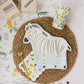 Zebra-shaped paper plates featuring a whimsical zebra illustration with gold foil accents. Includes 8 plates, approximately 11" wide and 10" tall. Perfect for adding a fun and wild touch to a safari-themed birthday party table decor.