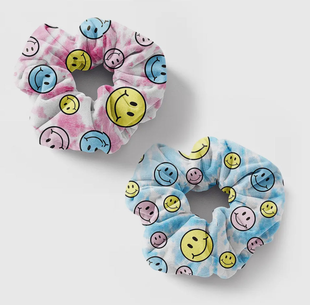 Two colorful scrunchies with smiley face patterns on a tie-dye background. One scrunchie features pink and blue tones, and the other blue and yellow, each adorned with various expressive smiley faces, adding a cheerful and playful touch to hair accessories.