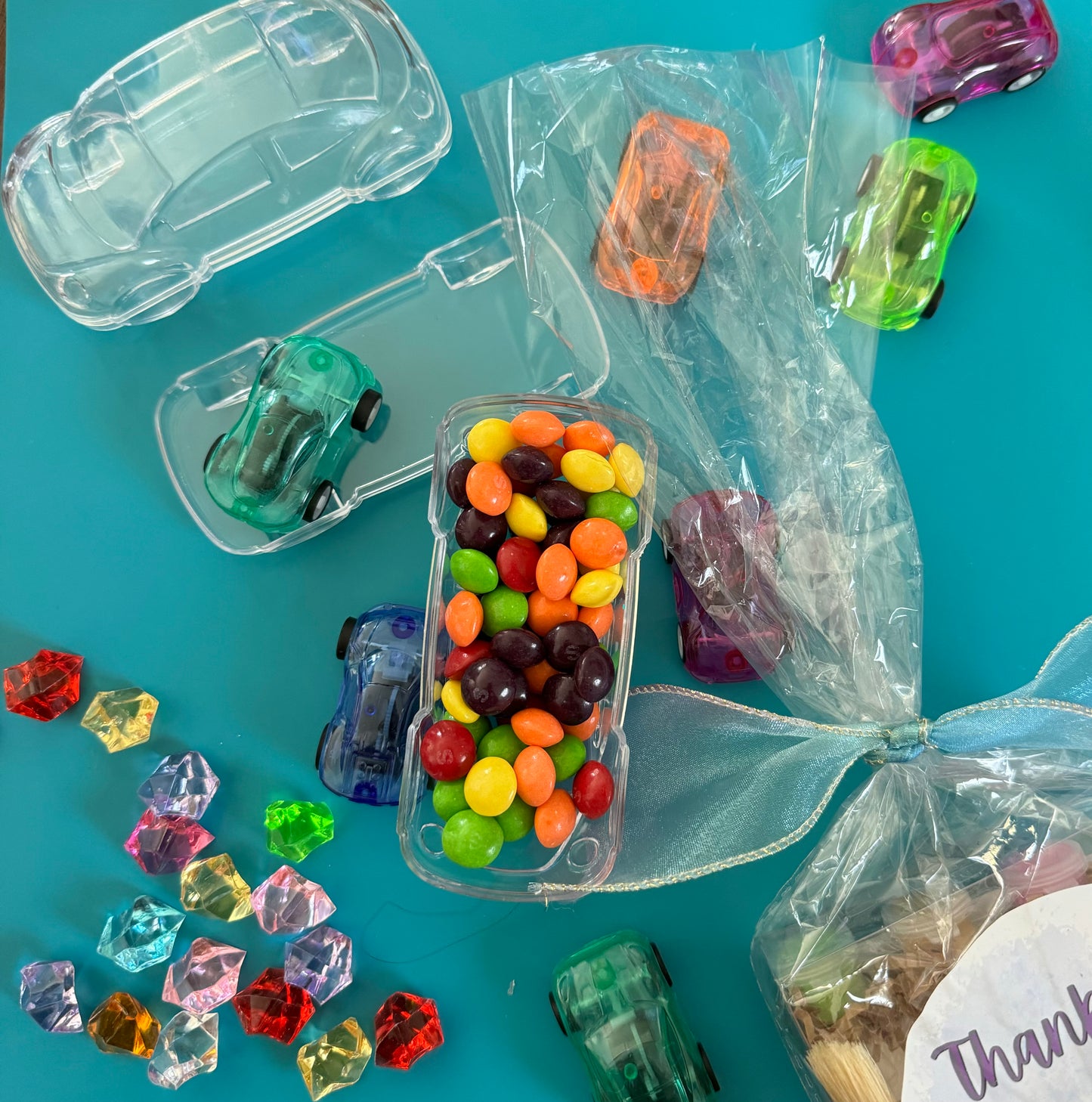 Car-themed candy favors, perfect for birthdays or playdates. Includes car-themed gummies or rainbow Skittles in a car-shaped box. Wrapped in cellophane with optional thank you label. Fun and delicious treat for any party. Custom candy containers available.