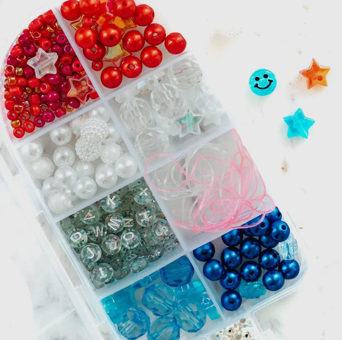 DIY jewelry bead kit featuring red, white, clear, and pearl beads, along with glitter alphabet beads and pink and clear string. Perfect for creating bracelets or necklaces. Made by a small, women-owned business. Warning: contains small parts.