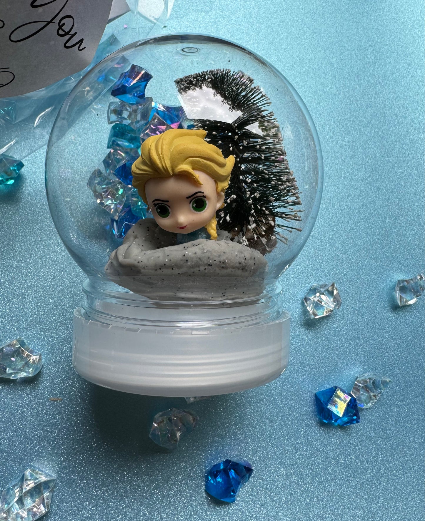 Frozen-themed sensory kit featuring snowy blue/white glitter swirl dough in a snow globe, Frozen figurines, soft snowy trees, snowmen, and glitter pompoms. Perfect for sensory development and creative play. Ideal for kids 3 and up. Choking hazard warning.