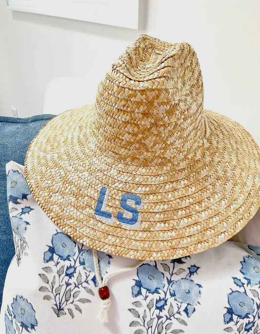 A stylish beach straw hat designed to provide shade at the beach or pool. The hat features a personalized touch with a custom monogram embroidered directly on it, adding a unique flair to your summer look.