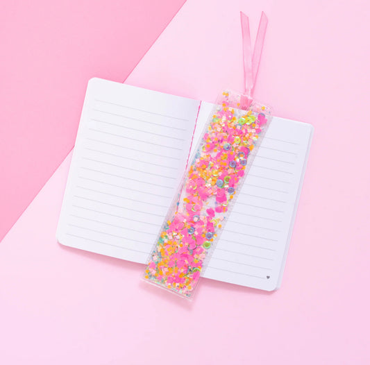 Fun confetti bookmark, perfect for book lovers. Measures 2" x 7", made from clear plastic with hand-selected, colorful confetti inside. Tied with a pink ribbon for an added touch of charm. Imported.