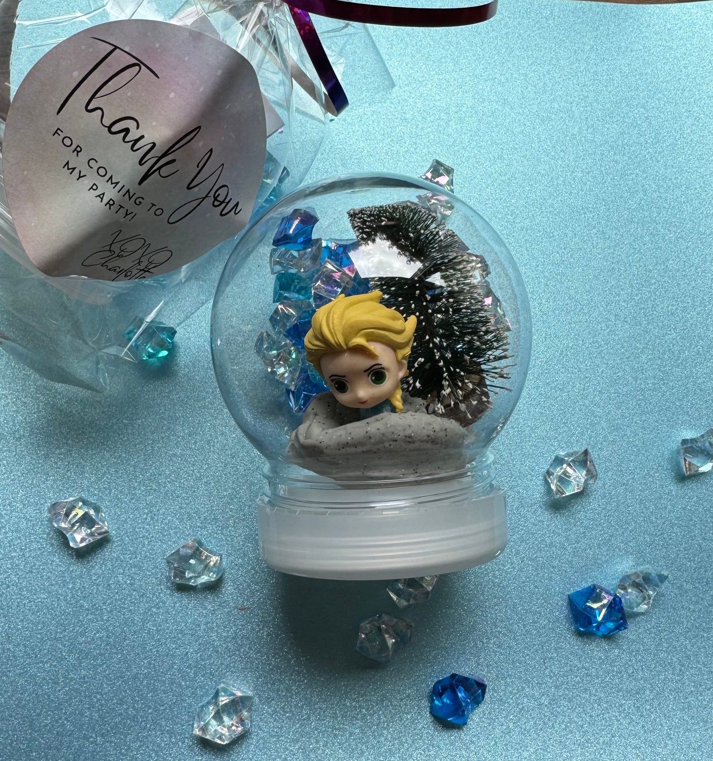 Frozen-themed sensory kit featuring snowy blue/white glitter swirl dough in a snow globe, Frozen figurines, soft snowy trees, snowmen, and glitter pompoms. Perfect for sensory development and creative play. Ideal for kids 3 and up. Choking hazard warning.