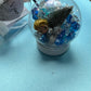 Frozen-themed sensory kit featuring snowy blue/white glitter swirl dough in a snow globe, Frozen figurines, soft snowy trees, snowmen, and glitter pompoms. Perfect for sensory development and creative play. Ideal for kids 3 and up. Choking hazard warning.