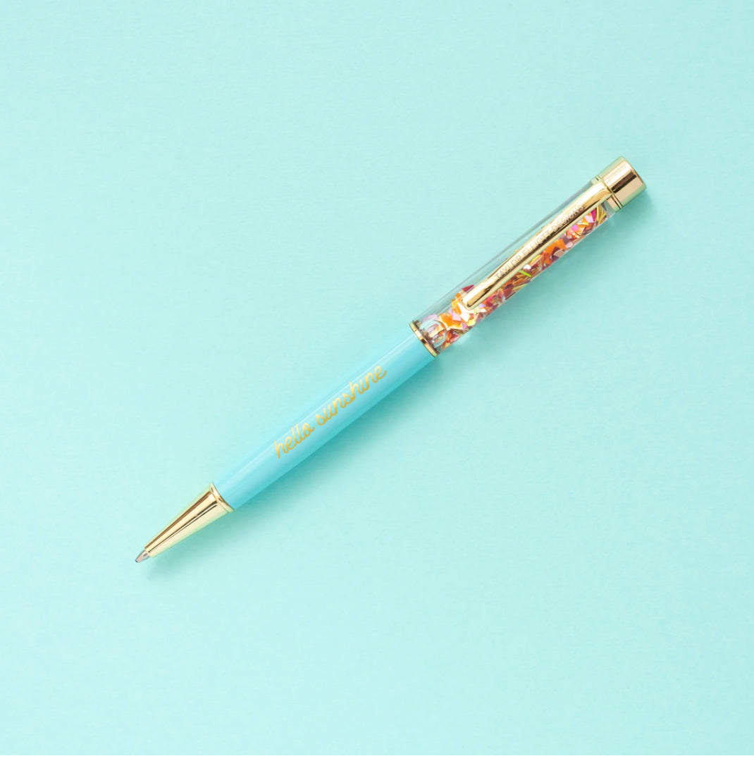 Confetti pen with gold metal accents, imprinted with 'Never let anyone dull your sparkle.' Medium ballpoint pen with black ink and a twist tip. Perfect desk accessory or gift, pairs well with notebooks. Features water-filled liquid inside for extra sparkle