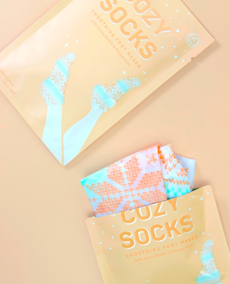 Cozy Socks Smoothing Foot Masks enriched with cocoa butter and peppermint oil, designed to hydrate and heal dry, cracked feet, featuring a fun fair isle print for a festive and relaxing self-care experience.