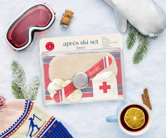 Pinch Provisions Aprés Ski Set, a 6-piece holiday gift set featuring a shot-ski with collapsible stainless steel shot glass, ivory sherpa sleep mask, scrunchie, mini hangover kit, and chic clear pouch with silver vegan trim. Perfect for Christmas 2024!