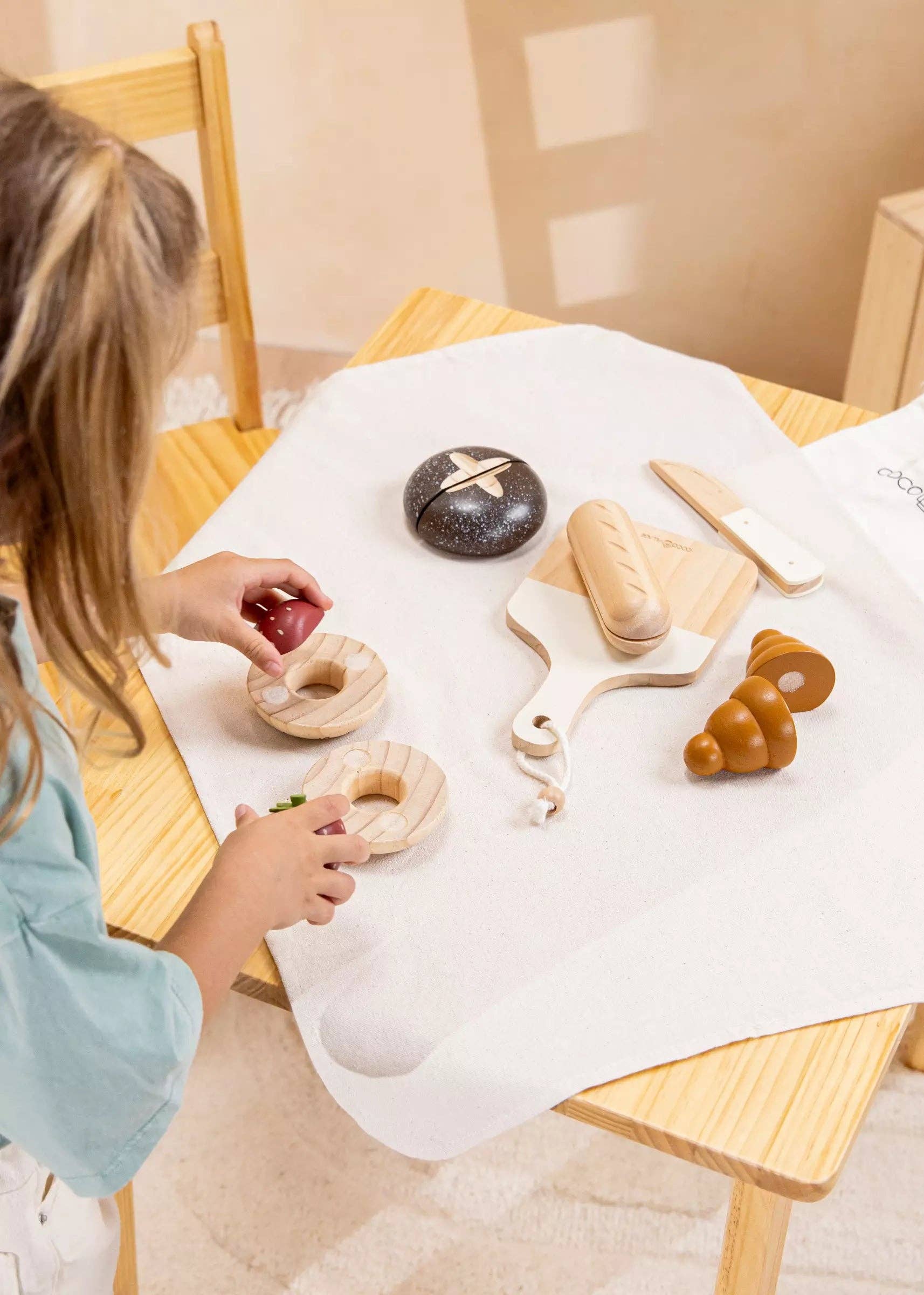 Wooden Bakery Playset for kids with baguette, croissant, pumpernickel, bagel, cutting board, and knife. Ideal for imaginative market play, helping children learn about different bread types, healthy eating, and colors. Perfect for pretend play with kitchen and market sets