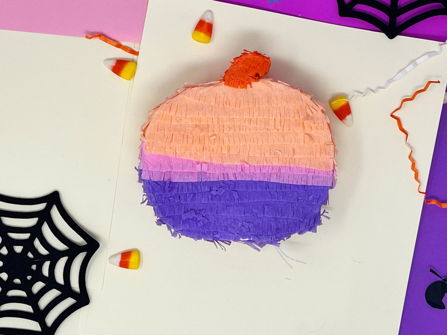 Groovy mini pumpkin piñata with orange, lavender, and pink colors for a boho Halloween vibe. Measures 5 inches tall and long, with a 1.5-inch width, featuring a trap door for treats. Perfect for Halloween decor or party favors for kids and family.